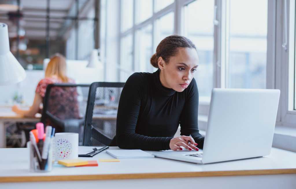 hip woman seated at desk working on laptop programming